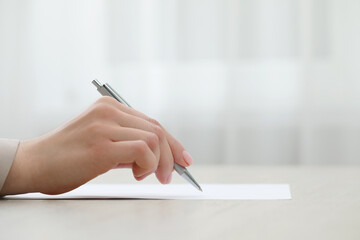 Woman writing on sheet of paper at table, closeup