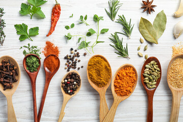 Spoons with different spices and herbs on white wooden table, flat lay