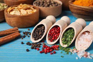 Scoops with different spices on light blue wooden table