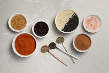 Bowls and spoons with different spices on light grey marble table, flat lay