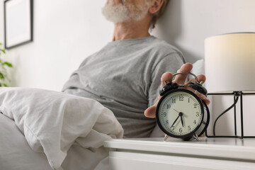 Man turning off alarm clock in bedroom, closeup