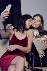 Cropped close-up shot of a lesbian couple takes a selfie on their phone. Girls with a bouquet of flowers smile and have a good time together. LGBT concept.