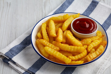 Homemade Unhealthy Crinkle French Fries with Ketchup on a Plate, low angle view.