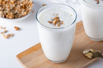 Kefir, buttermilk or yogurt with granola. Yogurt in glass on white wooden background.