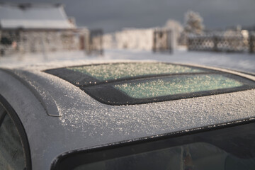 Modern car roof covered with snow on a sunny winter day. The panoramic sunroof in the winter.