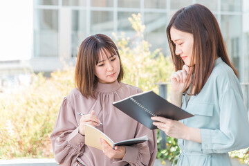 ビルの前でノートを見ながら勉強するアジア人大学生・ビジネスウーマン
