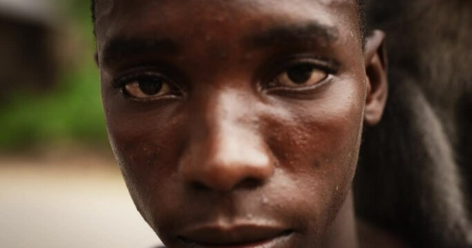 Close Up Portrait of an Authentic African Man Looking at the Camera and Carrying a Little Monkey on his Shoulder with Greenery in the Background. Indigenous Black Male Showing Harmony with Nature. 