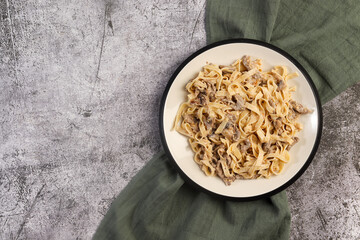 Homemade Beef Stroganoff Fettuccine Pasta with Whole Grain Mustard on a white round plate on a dark grey background. Top view, flat lay