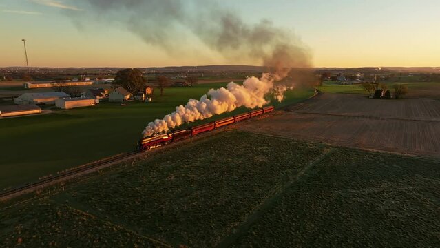 Drone View of a Steam Engine Approaching Blowing Smoke at Sunrise Traveling Thru the Farmlands