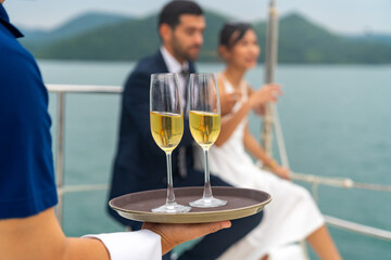 Asian man waiter serving champagne to passenger tourist while private catamaran boat yacht sailing...