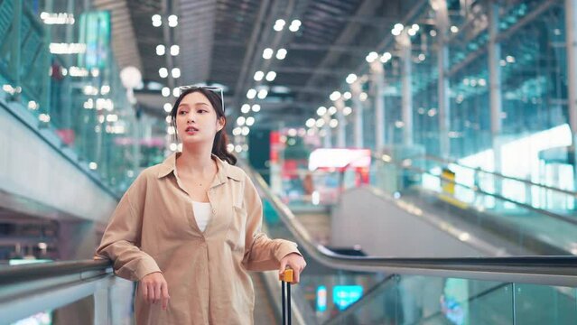Asian tourist woman traveller with simple suitcase stand on moving walkway in airport terminal, Tourist journey trip concept