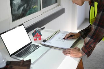 Cropped shot of engineer man working with blueprints and checking schedule on his laptop computer