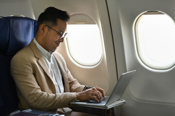Millennial businessman in stylish suit working with laptop in aircraft cabin during his business travel