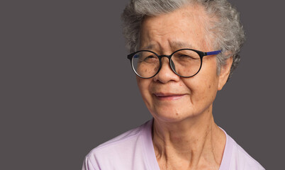 Beautiful elderly Asian woman looking at the camera with a smile while standing on a gray background