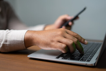 Hand typing on laptop while looking at smartphone