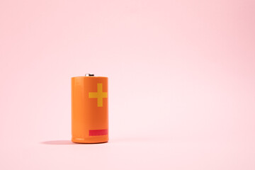 Orange battery on pink background, energy concept