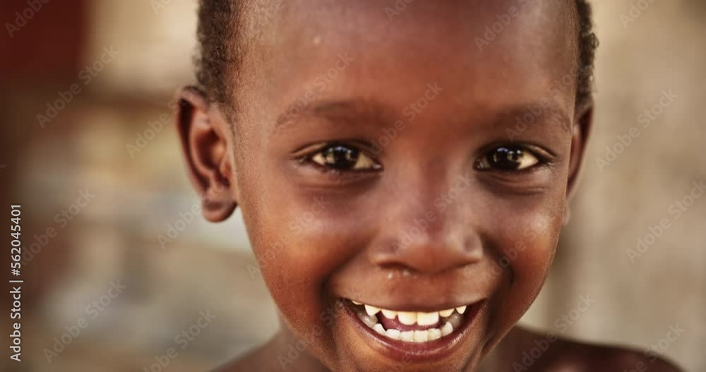 Wall mural close up portrait of a shy authentic african boy smiling and laughing at the camera with a blurred b