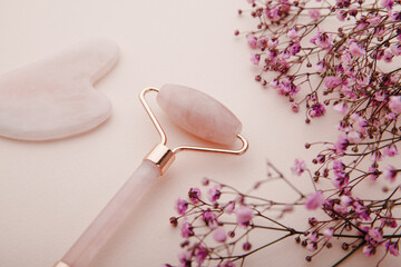 Face roller and gua sha massager made from natural jade stone on a pink background. Self facial massage concept