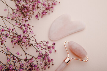 Face roller and gua sha massager made from natural jade stone on a pink background. Beauty care and anti-aging concept
