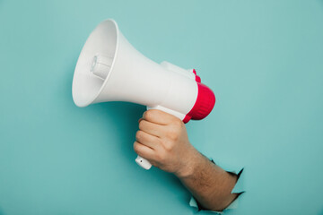 Man's hand arm hold megaphone isolated through torn blue background