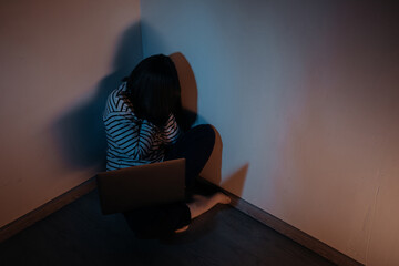 Young teenager female girl sitting with a laptop and crying in a dark room, concept of cyber...