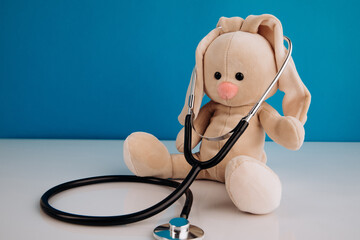 Bunny toy with a stethoscope on a blue background. Children's illnesses concept