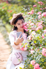 Fototapeta premium Beautiful woman holding a bouquet of roses and make selfie by smartphone in the garden. Happy woman smelling rose and taking selfie with smartphone. Valentine's day concept,Selfie of happy of smiling.