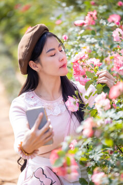 Beautiful woman holding a bouquet of roses and make selfie by smartphone in the garden. Happy woman smelling rose and taking selfie with smartphone. Valentine's day concept,Selfie of happy of smiling.