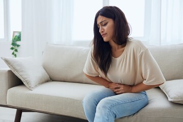 Woman sitting on sofa at home back and stomach pain during menstruation, women's day, women's health problems, suspected appendicitis