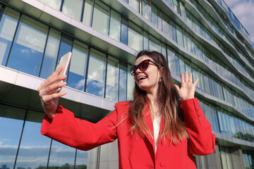 A businesswoman in a red stylish jacket during a video call with colleagues on the background of the office outside