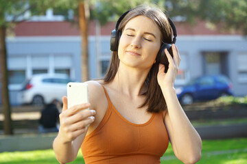 Beautiful young woman listening to music on her headphones outside in city