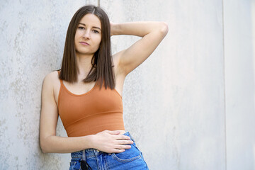 Fototapeta na wymiar Young beautiful woman in summer clothes leans against a concrete wall for a portrait