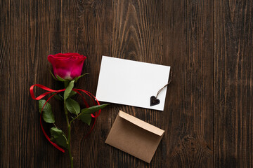 Red rose with postcard on wooden background. Happy Valentines Day postcard. Love concept for mothers day or valentines day. Valentine card with space for text