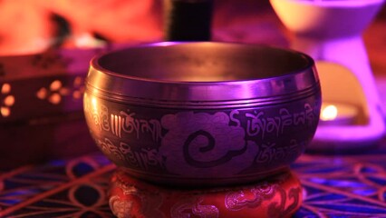 Tibetan singing bowl meditation by hand rotation with pinkish colored lights with candle and incense in the background