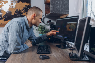 Side view of male video maker editing video using professional software while pointing at computer screen in home office 