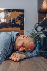 Tired male freelancer sleeping on table after hard working day in home studio  
