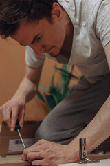Fototapeta na wymiar Focused man tightening bolt with screwdriver during process of furniture assembly at home 