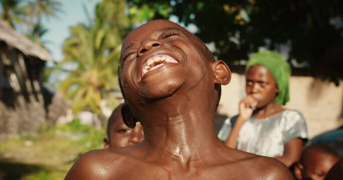 Close Up Portrait of a Playful Authentic African Kid Looking at the Camera and Laughing with Other Kids in the Background. Happy Energetic Black Boy Sharing his Beautiful Big Smile with the World