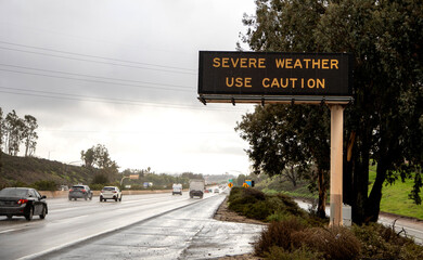 Digital sign at freeway stating Severe Weather Use Caution with wet freeway and traffic. The image...