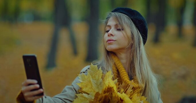 female blogger take selfie with yellow leaves bunch in park in autumn, smiling to camera, 4K, Prores