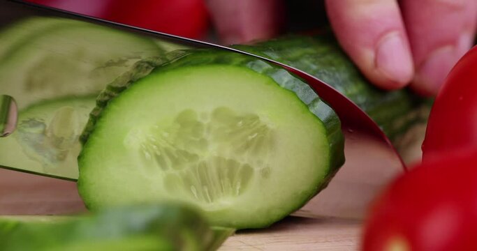 Slice a green ripe cucumber in thin circles, washed a long green cucumber during slicing for salad