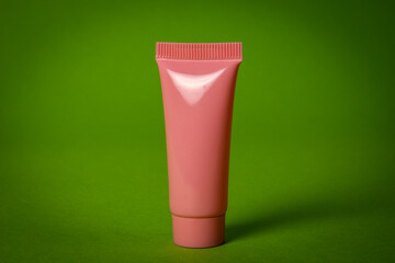 Pink cosmetic tube on green background with copy space. Skin care, body treatment, beauty concept