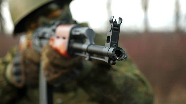 Muzzle of a machine gun close-up, blurred background of a man. A soldier in a military camouflage uniform holds a machine gun and takes aim. Military conflict. War. Military operation.