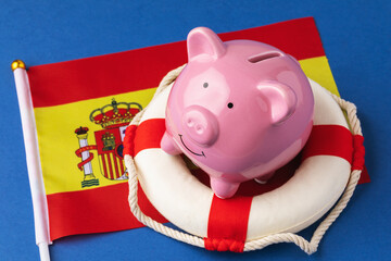 Piggy bank, lifebuoy and flag on a blue background, concept on the theme of saving the Spanish...