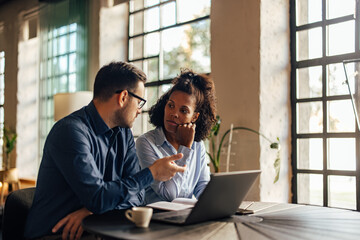 Male boss having a meeting with his female client, using a laptop, having a conversation.