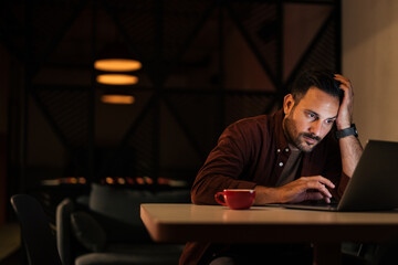 Focused man working on the new project, over the laptop, late at night.