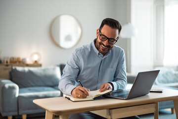 Obraz premium Smiling businessman taking notes in the notebook, sitting at the home office.