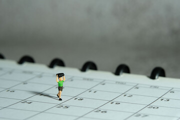 Miniature people toy figure photography. A boy running above monthly planner calendar. Grey cloudy...