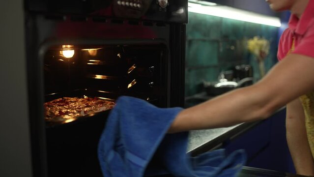 A man in an apron prepares dinner and takes a hot pizza out of the oven. Evening in the blue kitchen, freshly prepared pizza. The man prepares food for the family. High quality 4k footage