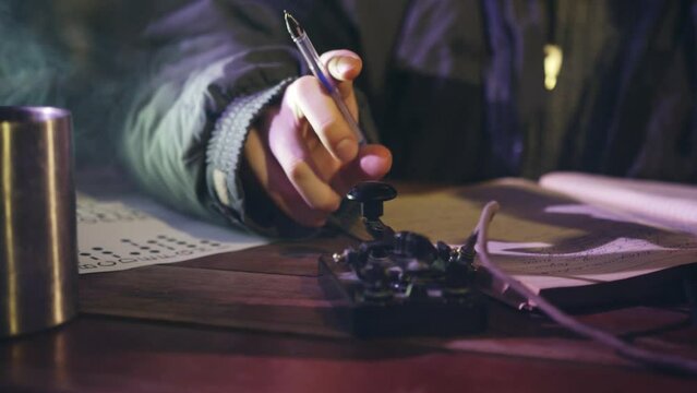 Man transmits information by telegraph sitting at table in dark room. Finger of male person tapping to communicate in Morse code closeup